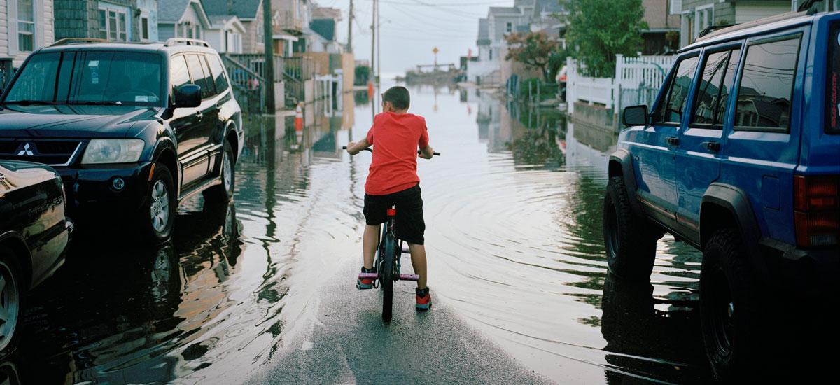 gw-sea-level-rise-boy-on-bike-looking-at-tidally-flooded-neighborhood